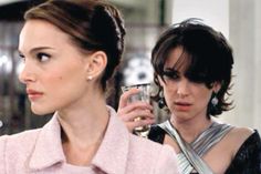 two women standing next to each other holding wine glasses in their hands and looking at something