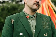 a man wearing a green jacket with flowers on his lapel and a red flower in his hair