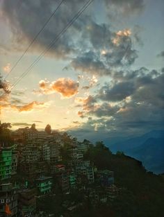 the sun is setting over a city on top of a hill with power lines in the foreground