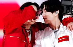 two people standing next to each other and one is holding a camera up to his face