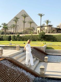 a woman is standing on some steps in front of an egyptian style pool and pyramids