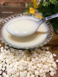 a spoon full of milk sitting on top of a bowl filled with small white beans