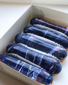 four decorated hot dogs in a box on a table with space theme frosting and sprinkles