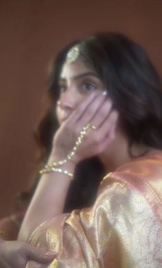 a woman in a gold sari covering her face with her hands and looking at the camera