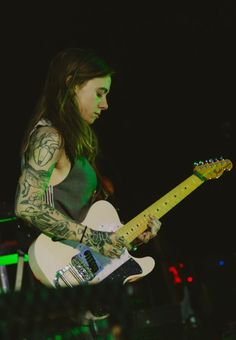 a man with long hair and tattoos playing an electric guitar on stage at a concert