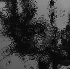 raindrops are seen in the water on top of a window pane with black and white background