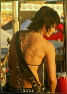 a man with no shirt on holding a guitar in his right hand and looking down at the ground