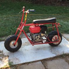 a small red motorcycle parked on top of a cement slab next to grass and bushes