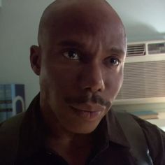 a close up of a person wearing a black shirt and tie with an air conditioner in the background