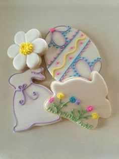 three decorated cookies sitting on top of a white plate next to a flower and an egg