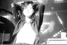 a woman standing in front of a keyboard on top of a stage with her hands behind her head