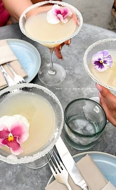 two people are holding glasses with drinks in them and one has a flower on the rim