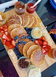 pancakes with fruit, strawberries and blueberries on a cutting board next to cups of juice