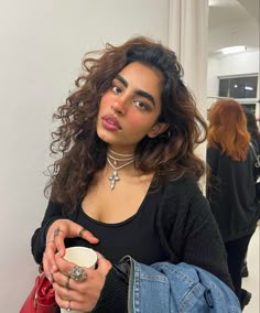 a woman holding a cup in her right hand and looking at the camera with an intense look on her face