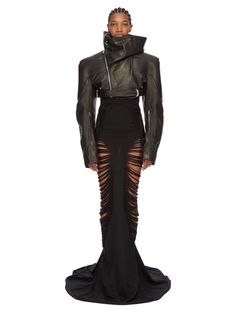 a woman wearing a black leather jacket and skirt with cutouts on the sides, standing in