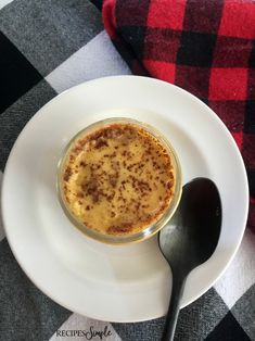 a white plate topped with a dessert on top of a checkered table cloth next to a spoon
