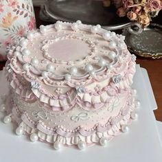 there is a large pink cake with pearls on the top and sides, sitting on a white platter