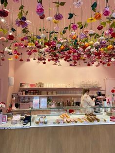 a woman behind a counter in a restaurant with lots of flowers hanging from the ceiling