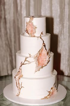 a three tiered white cake with pink flowers on it's side and frosting