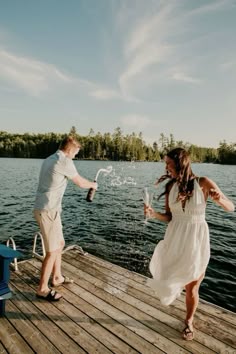 a man and woman standing on a dock with water splashing from their hands as they laugh