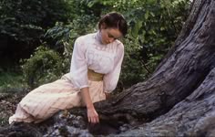 a woman sitting on the ground next to a tree