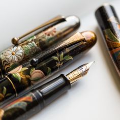 two pens sitting next to each other on top of a white surface with flowers painted on them