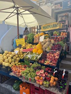 an outdoor market with lots of fresh fruits and vegetables on display for sale under an umbrella