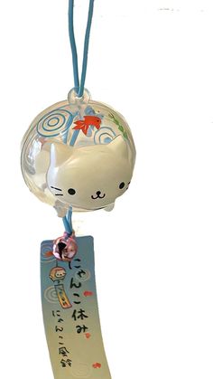 a white cat ornament hanging from a blue cord with writing on it's side