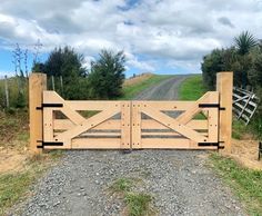 a wooden gate on the side of a dirt road with grass and trees in the background