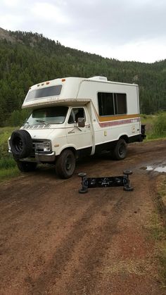 an rv parked on the side of a dirt road in front of a wooded area