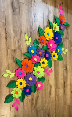 colorful paper flowers are arranged on a wood floor with green leaves and red, yellow, blue, pink, orange, and purple flowers