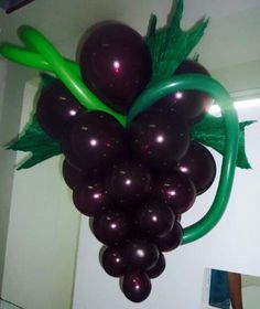 a bunch of grapes hanging from the ceiling with green leaves on it's stem