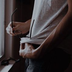 a man wearing glasses standing next to a window with his hands on his hips and looking out the window