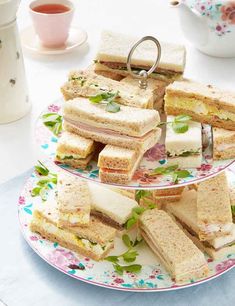 three tiered plates with sandwiches on them next to cups and teapots in the background