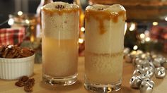 two glasses filled with liquid sitting on top of a table next to silver bells and christmas decorations