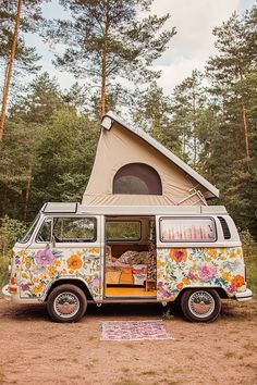 an old van with flowers painted on it parked in front of a tent and trees