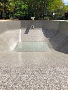 an empty swimming pool in the middle of a park with trees and bushes behind it