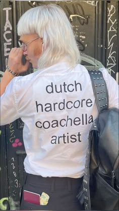 a woman with white hair talking on a cell phone while wearing a t - shirt that says dutch hard core coachella artist