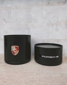 two black porsche planters sitting next to each other on a tile floor in front of a wall