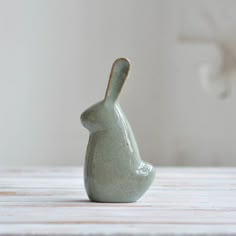 a small ceramic rabbit figurine sitting on top of a wooden table next to a white wall