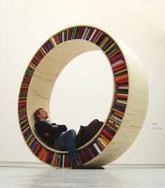 a man is sitting in a circular bookcase with his feet on the floor and reading