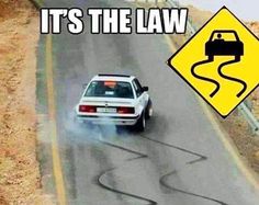 a white car driving down a road next to a sign that says it's the law