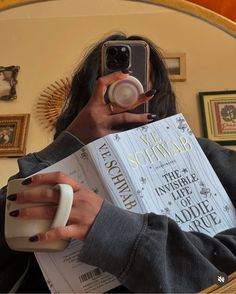a woman taking a selfie with her cell phone and holding a book in front of her face