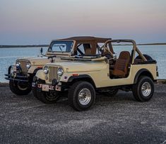an old jeep is parked by the water