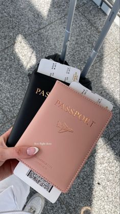 a person holding a pink passport case in front of their hand and luggage behind them