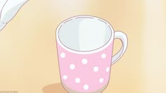 a pink and white polka dot coffee mug on a tan surface next to a banana