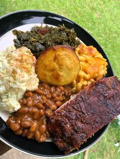 a black plate topped with meat, beans and other foods on top of a green lawn