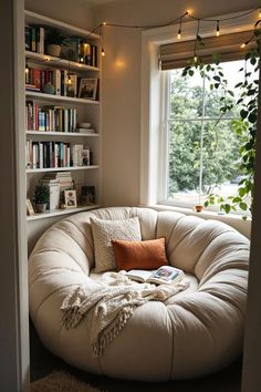 a white bean bag chair in front of a window with bookshelves and plants