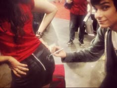 a man standing next to a woman in a red shirt and black leather pants with her hands on her hips