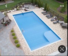 an aerial view of a swimming pool surrounded by lawn chairs and trees in the background
